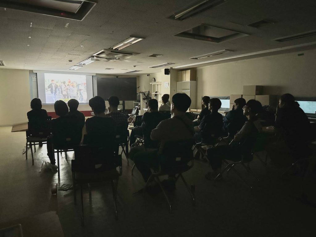 어둠 속에서 불을 밝힌 스크린을 지켜보는 여러 사람들의 뒷모습 사진. 