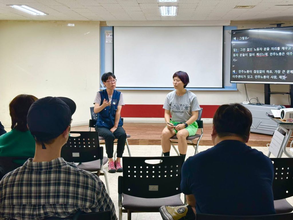 무대 앞 초대손님과 진행자의 모습, 그리고 그 둘을 지켜보는 청중의 뒷모습. 