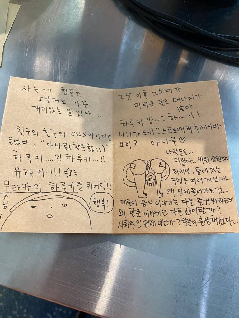 진zine 일부 단면 사진_다음은 텍스트 전문_왼쪽면_사는 게 힘들고 고달퍼도 가끔 재미있는 일있다...... 친구의 친구의 SNS 아이디를 들었다.... 아나루(항문핥기) 하루키..,,(물음표 느낌표) 유래카(느낌표느낌표느낌표 별똥별 샤랄라. 무라카미 하루키를 퀴어링(느낌표느낌표) 글자 아래 단순 선으로 눈코입 얼굴 머리칼이 그려진 뚱한 표정의 사람 얼굴, 그 옆에는 말풍선으로 행복. 오른쪽면_그날 이후 그 노래가 머리를 돌고 떠나지가 않다. 하루키짱(물결표 물음표) 하아이(느낌표) 나니가스키(물음표) 스토로배리후레이바 요리모 아나루(하트) 사람들은,,, 더럽다... 비위 상한다... 하지만. 몸에 있는 구명은 여러 개인데,.. 왜 입에 들어가는 것,.... 예를 들어 음식 이야기는 다들 즐거워 하는데 왜 항문 이야기는 다들 싫어할까(물음표) 사회적인 규제 아닌가(물음표) 항문이 불쌍해졌다,... 페이지 가운데 단순선으로 그려진 인물 그림 선 채로 고개를 숙여 가랑이 사이로 내려온 머리칼과 얼굴이 보인다. 양손으로 궁둥이를 벌리니 항문과 성기도 마땅히 있어야 할 곳에 그려져 있다.