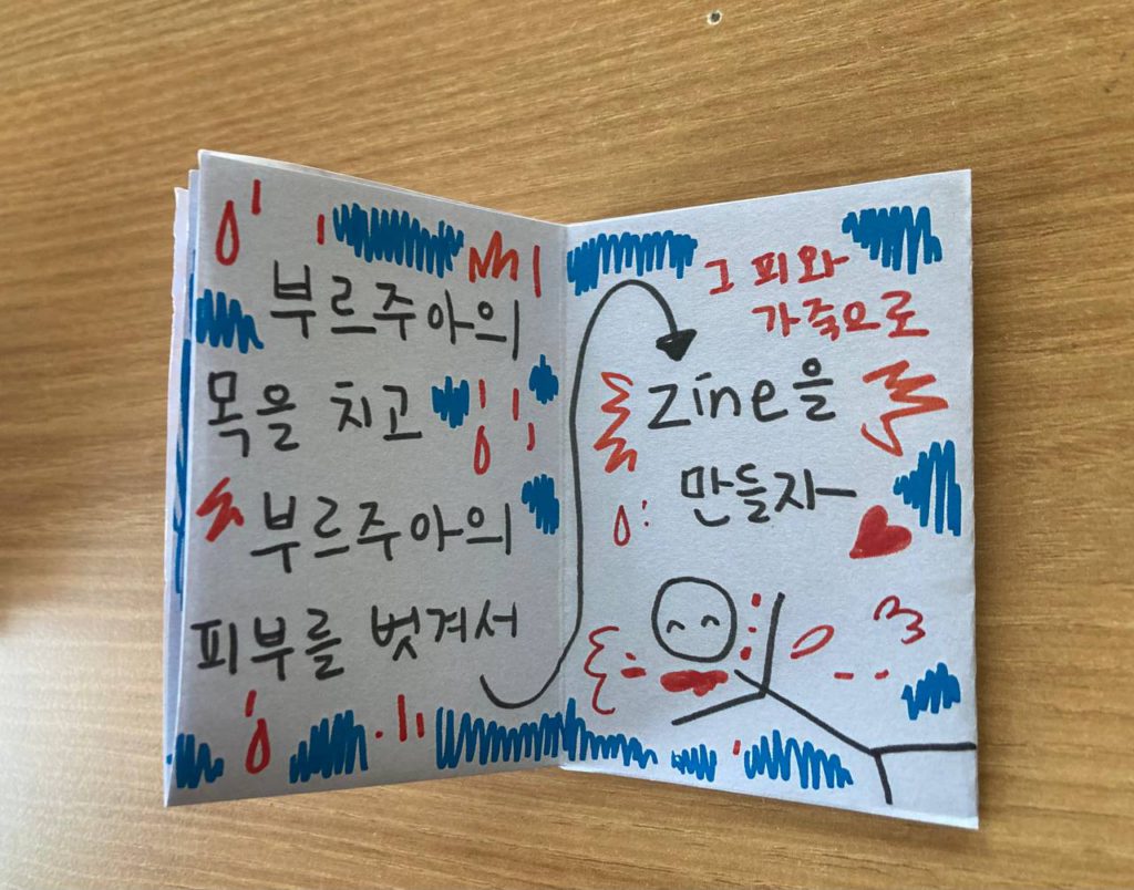 진zine 일부 단면 사진_빨갛고 파란 채색선들 사이로 굵은 검정 손글씨가 쓰여 있다. '부르주아의 목을 치고 부르주아의 피부를 벗겨서 그 피와 가죽으로 zine을 만들자' 철퍽 엎어진 사람이 웃으며 목에 피를 흘리는 단순 선으로 이루어진 그림.