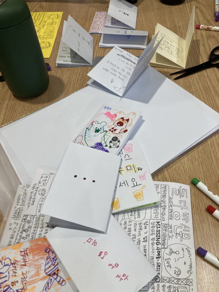 테이블 위에 옹기종기 모인 진 결과물들 사진. 책상 위에는 가위와 컬러 수성펜 등이 놓여 있다.