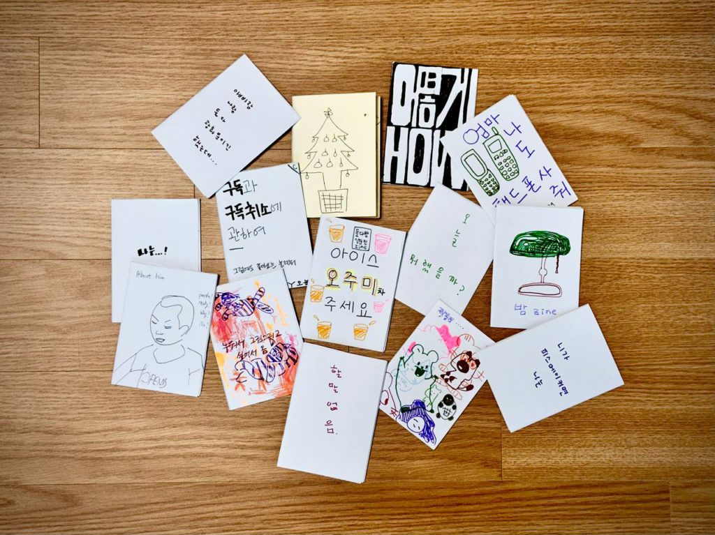 에이포용지를 접고 접어 같은 규격으로 만들어진 저마다 다른 손글씨와 손그림으로 채워진 다양한 표지의 진 결과물들이 모인 사진. 