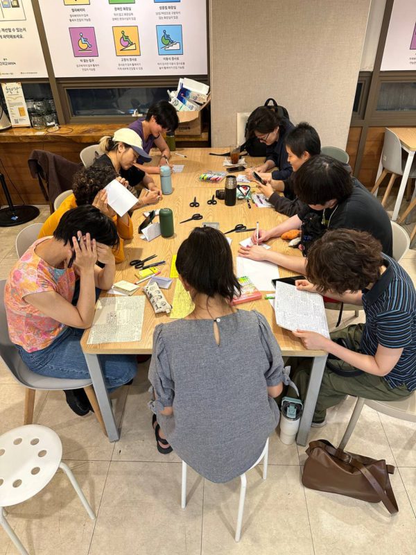 들다방 한쪽 테이블에 옹기종기 모여 진을 제작중인 사람들 사진. 책상 위에는 가위와 컬러 수성펜, 개인 컵 등이 놓여 있다.