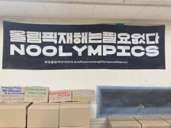 검정 가로 현수막. 한글과 영문이 두 줄 가로쓰기 돼 있다. 상단. 올림픽 재해는 필요없다. 하단 NO OLYMPICS. 그 밑에 색색가지 손글씨로 오밀조밀 작게 쓰인 손피켓 네 개.