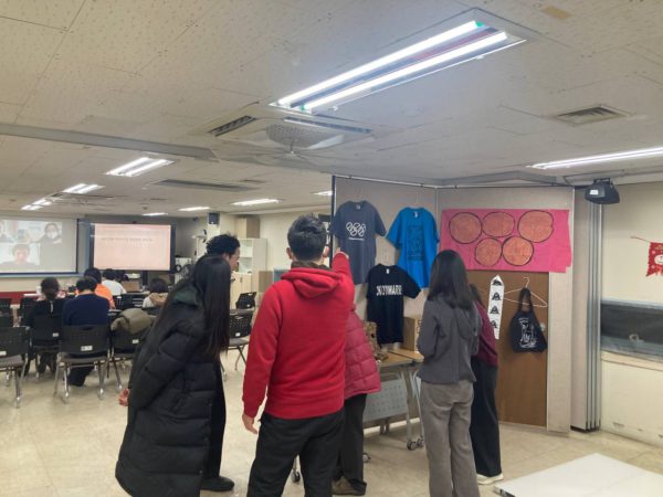 들다방 상영회장 풍경. 앞쪽 스크린에 화상회의 줌 미팅 창이 열려 있고, 의자에 앉은 사람들. 상영회장 뒤편에는 각종 올림픽반대 티셔츠와 가방, 플래그 등 굿즈 들이 전시돼 있다.