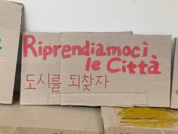 한글과 이탈리아어로 쓰인 빨강 손피켓. 도시를 되찾자. Riprendiamoci le Città.