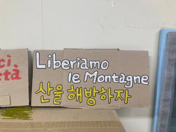 한글과 이탈리아어로 쓰인 노랑 손피켓. 산을 해방하자. Liberiamo le Montagne.