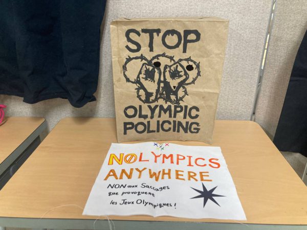 스톱 올림픽 폴리싱이라 적힌 종이 봉투 가면과 천으로 만든 손피켓. 노 올림픽스 애니웨어라 쓰여 있다.