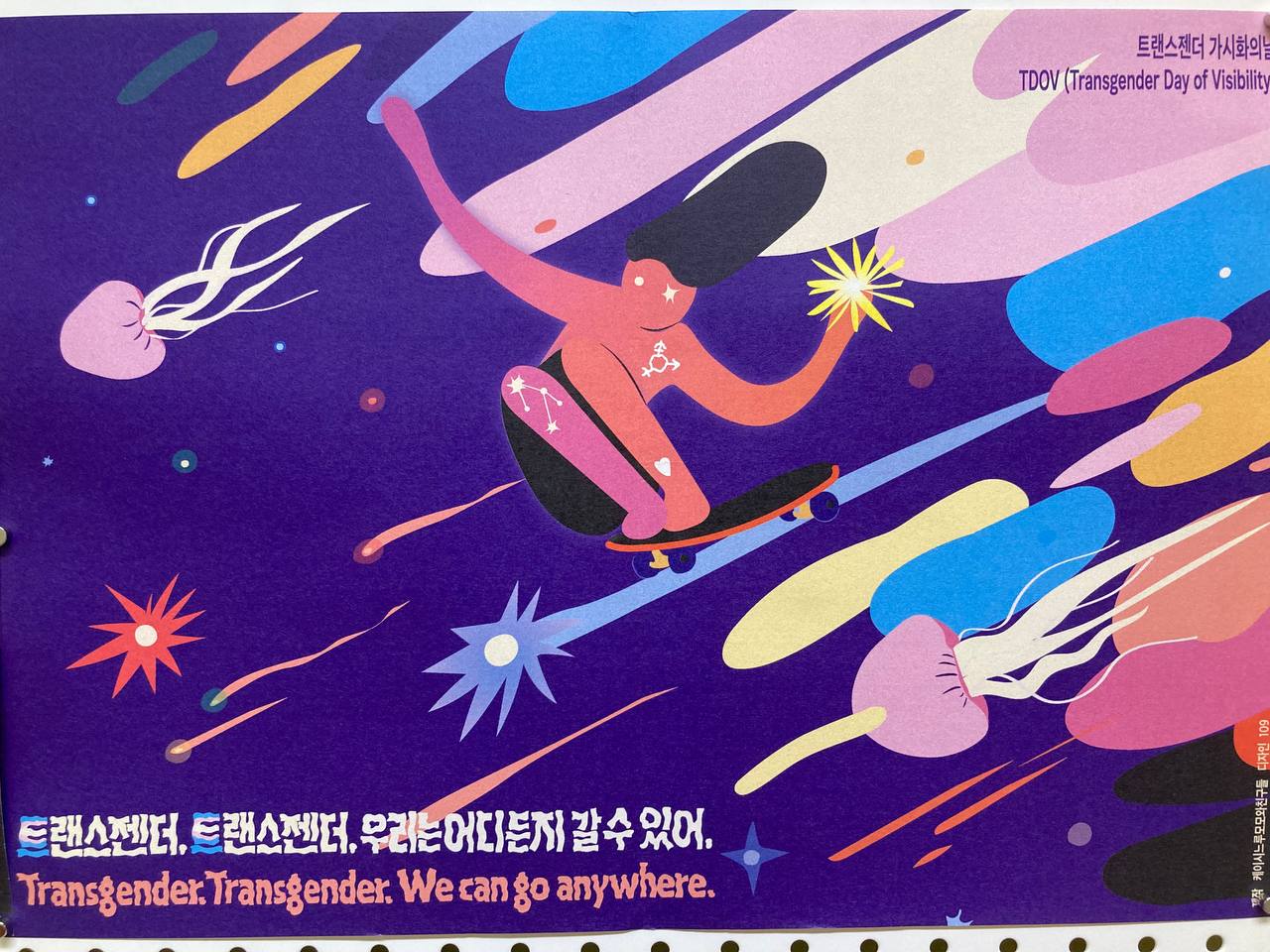 이번 케이시-느루-모모와 친구들에서 배포한 트랜스젠더 가시화 포스터 전면 촬영 사진. 보라색 바탕 위에 트랜스젠더 자긍심을 나타내는 플래그(깃발) 상징색 파랑, 분홍, 하양이 생명 그리고 비생명의 여러 외연을 띤 채 신나게 미끄러져 나아가는 이미지. 다음은 텍스트 전문. '트랜스젠더, 트랜스젠터, 우리는 어디든지 갈 수 있어.