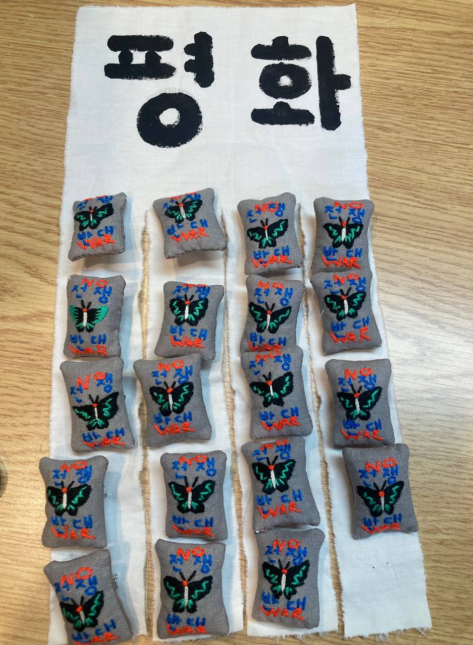 전쟁 반대 수공예 뱃지 약 20개가 주르르 질서정연하게 흰 천에 매달려 있는 모습